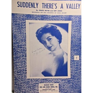 May include: Sheet music cover for "Suddenly There's a Valley" by Chuck Meyer and Biff Jones, recorded by Gogi Grant. The cover features a black and white photo of Gogi Grant with her signature, set against a blue patterned background.