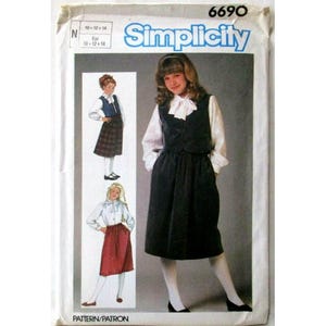 以下が含まれることがあります： Simplicity 6690の裁縫型紙封筒。ベストとスカートのセットアップのイラストが描かれています。メイン画像は、リボン付きの白い長袖ブラウスの上にダークカラーのベストを重ね、ダークカラーのスカートを合わせたスタイルです。2つの小さな挿絵でバリエーションが示されています。
