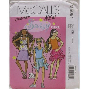 Op de afbeelding: Een roze McCall's naaipatroon envelop met illustraties van drie meisjes in stijlvolle outfits. De tekst bevat "CHECKET NEW SASSY GIRL" en patroonnummer M5091. Maat CH (7-8-10) is aangegeven.