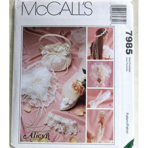 May include: McCall's sewing pattern featuring bridal accessories. The image shows a heart-shaped ring pillow, a lace garter, a satin purse, a shoe with a rose, and other bridal items. The pattern number is 7985.