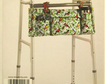 May include: A walker bag featuring a vibrant bird and foliage design. The bag, attached to a silver walker, has several pockets. A black travel mug and a small electronic device are visible within the pockets.