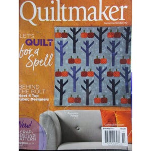 Puede incluir: La portada de la revista Quiltmaker presenta un diseño de edredón con calabazas naranjas y árboles azules sobre un fondo gris. Se muestra el texto "LET'S QUILT for a Spell". La revista también incluye el texto "Pumpkin Forest" y "Meet 4 Top Fabric Designers".