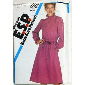 May include: A Simplicity sewing pattern envelope 5639 for a long-sleeved, midi-length dress in a solid magenta colour. The dress features a high collar, a front zip closure, and a waist tie. The envelope displays the text 5639, $1.50, and £1.35.