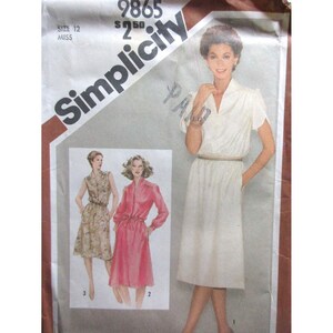 May include: Simplicity sewing pattern 9865, size 12 Miss. The pattern features illustrations of three different dress designs. The main image shows a woman wearing a white dress with short sleeves and a belt. The pattern's logo is in the upper left corner.