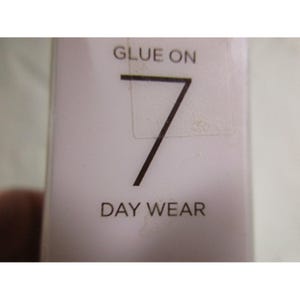 Puede incluir: Primer plano de un envase de producto blanco con las palabras "GLUE ON" en la parte superior y "7" en una fuente negra grande. Debajo del n&uacute;mero est&aacute; el texto "DAY WEAR".
