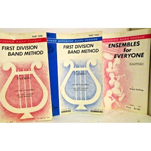 Puede incluir: Tres libros de métodos de banda vintage. Las portadas presentan una ilustración de lira y texto que incluye "First Division Band Method" y "Ensembles for Everyone". Los libros son de color rojo, azul y rosa, con texto en blanco y negro.