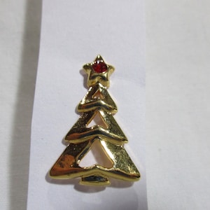 May include: A gold-coloured Christmas tree pin with a red rhinestone star on top.