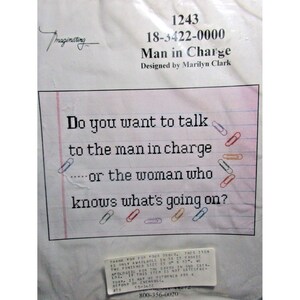 May include: A white package with the text "Man in Charge" and the question "Do you want to talk to the man in charge or the woman who knows what's going on?" The design includes paperclips.