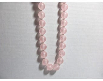 May include: A necklace composed of round, light pink beads. The beads are strung together, forming a U-shape against a white background. The beads appear to be made of a translucent material.