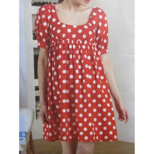 Puede incluir: Vestido rojo con lunares blancos. El vestido tiene mangas cortas y un escote cuadrado. La tela está fruncida en la cintura, creando una falda fluida. El vestido llega a la rodilla y parece estar hecho de un material ligero.