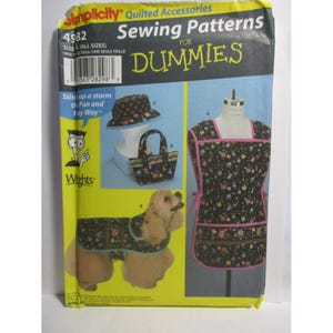 May include: Simplicity sewing pattern for quilted accessories, including a hat, tote bag, apron, and dog coat. The pattern features a black floral design with pink accents. The package includes the text "Sewing Patterns for Dummies."