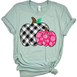 May include: A light blue t-shirt with a black and white checkered pumpkin and a pink pumpkin with a floral design.