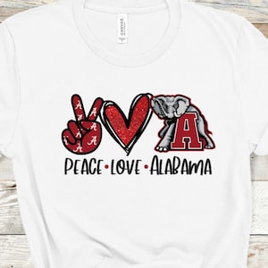 May include: White t-shirt with a red peace sign, a red heart, and a red Alabama elephant with the text "Peace Love Alabama".