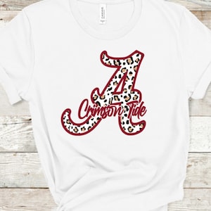 May include: White t-shirt with a red outline of the letter "A" with a leopard print pattern. The text "Crimson Tide" is written in a cursive font inside the letter.