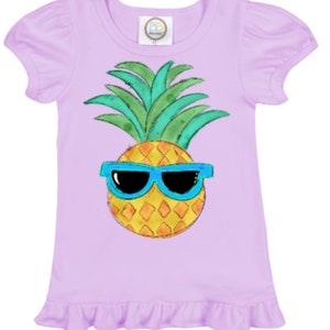 May include: A lavender short-sleeved shirt with a ruffle hem features a cartoon pineapple wearing blue sunglasses.