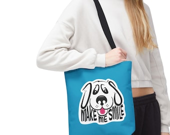 Könnte beinhalten: Eine türkisfarbene Tragetasche mit schwarzem Riemen zeigt ein weißes und schwarzes Cartoon-Hunde-Gesicht mit den Worten "MAKE ME SMILE". Die Tasche wird von einer Person getragen, die einen weißen Kapuzenpullover und eine schwarze Hose trägt.