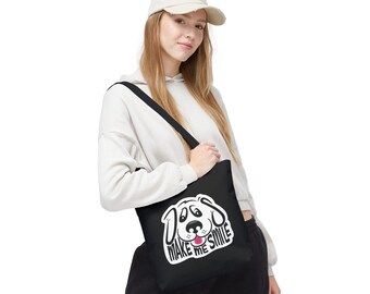 Könnte beinhalten: Schwarze Tragetasche mit einem Cartoon-Hunde-Gesicht und dem Text "Dogs Make Me Smile" in Weiß. Die Tasche hat einen schwarzen Schulterriemen. Ein lustiges und fröhliches Accessoire für den täglichen Gebrauch.