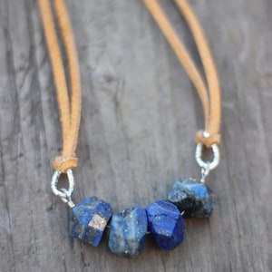 May include: A necklace with a suede cord and a row of five faceted lapis lazuli stones. The stones are a deep blue color with flecks of gold.