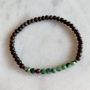 Könnte beinhalten: Ein braunes Holzperlenarmband mit einer Reihe grüner und rosafarbener Edelsteinperlen.