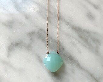 May include: A light blue gemstone pendant necklace on a brown cord.