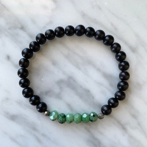 Könnte beinhalten: Ein schwarzes Perlenarmband mit einer Reihe grüner Edelsteinperlen in der Mitte.