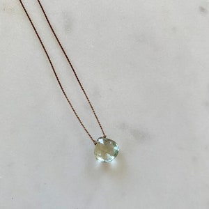 May include: A delicate necklace with a light green gemstone pendant on a brown cord.
