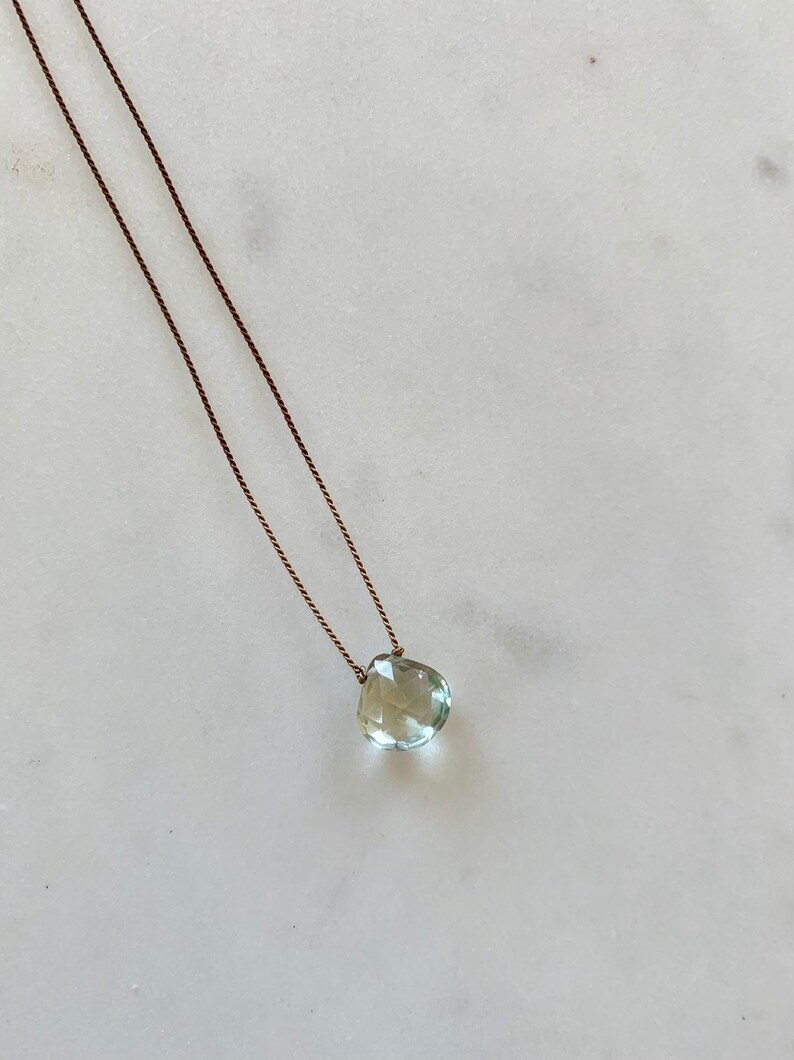 May include: A delicate necklace with a light green gemstone pendant on a brown cord.