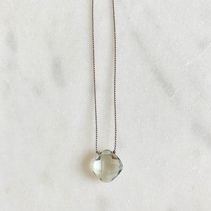 May include: A delicate necklace with a light green gemstone pendant on a brown cord.