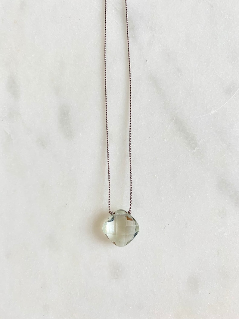 May include: A delicate necklace with a light green gemstone pendant on a brown cord.