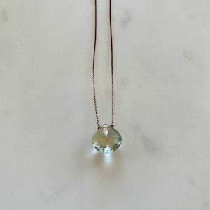 May include: A delicate necklace with a light green gemstone pendant on a brown cord.