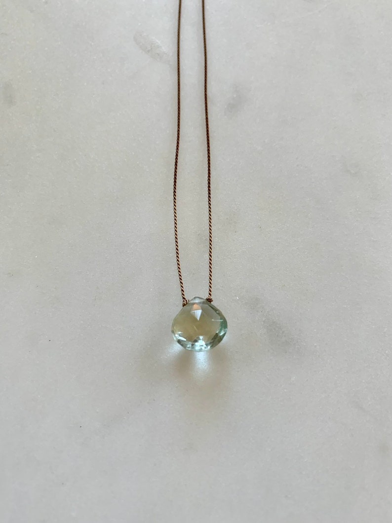 May include: A delicate necklace with a light green gemstone pendant on a brown cord.