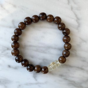 Könnte beinhalten: Ein braunes Holzperlenarmband mit einem klaren Kristall-Akzent.