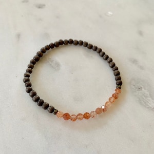 May include: A brown wooden beaded bracelet with a row of light brown sunstone beads.