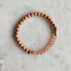 May include: A wooden and sunstone beaded bracelet. The bracelet is made with natural wood beads and orange sunstone beads.