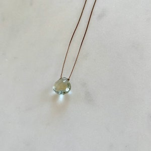 May include: A delicate necklace with a light green gemstone pendant on a brown cord.