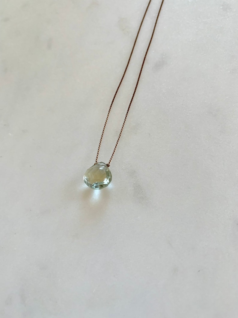 May include: A delicate necklace with a light green gemstone pendant on a brown cord.