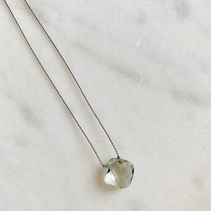May include: A delicate necklace with a light green gemstone pendant on a thin gray cord.