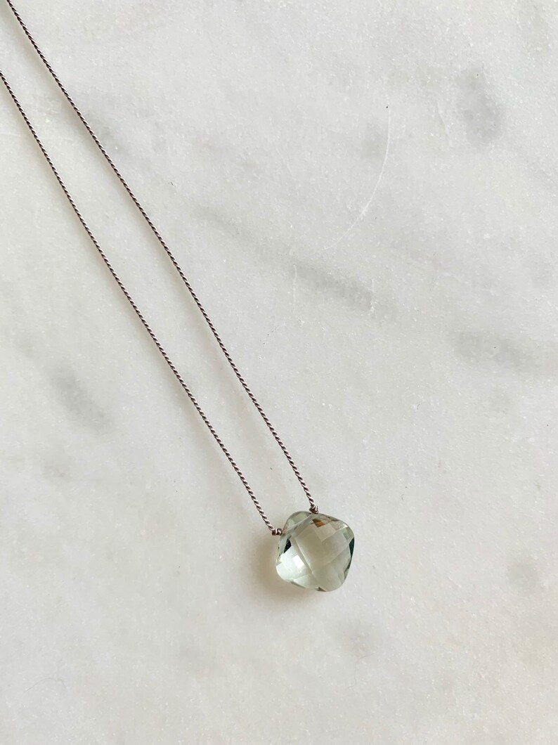 May include: A delicate necklace with a light green gemstone pendant on a thin gray cord.