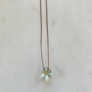 May include: A delicate necklace with a light green gemstone pendant on a brown cord.