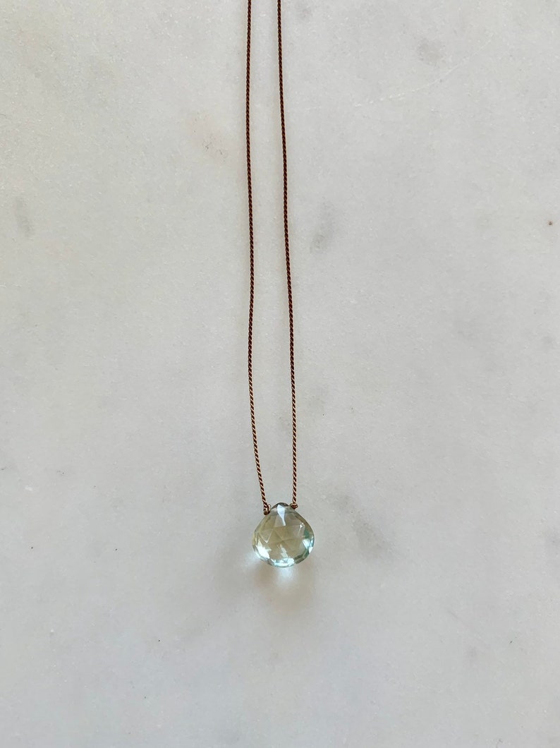 May include: A delicate necklace with a light green gemstone pendant on a brown cord.