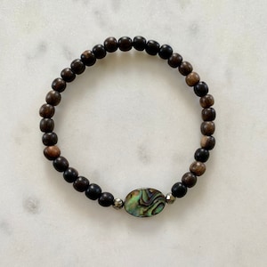 Könnte beinhalten: Ein dunkelbraunes Holzperlenarmband mit silbernem Akzent und einem grünen und braunen Abalone-Muschel-Anhänger.