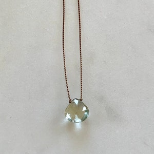 May include: A delicate necklace with a light green gemstone pendant on a brown cord.