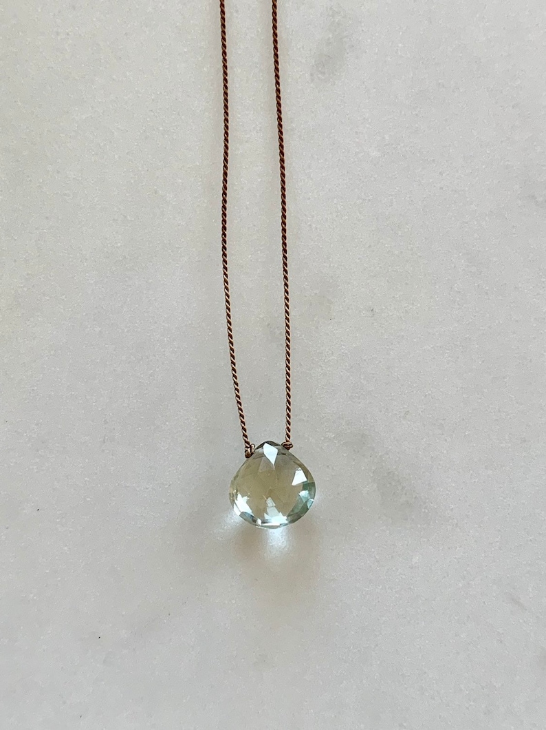 May include: A delicate necklace with a light green gemstone pendant on a brown cord.