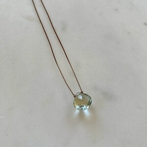 May include: A delicate necklace with a light green gemstone pendant on a brown cord.