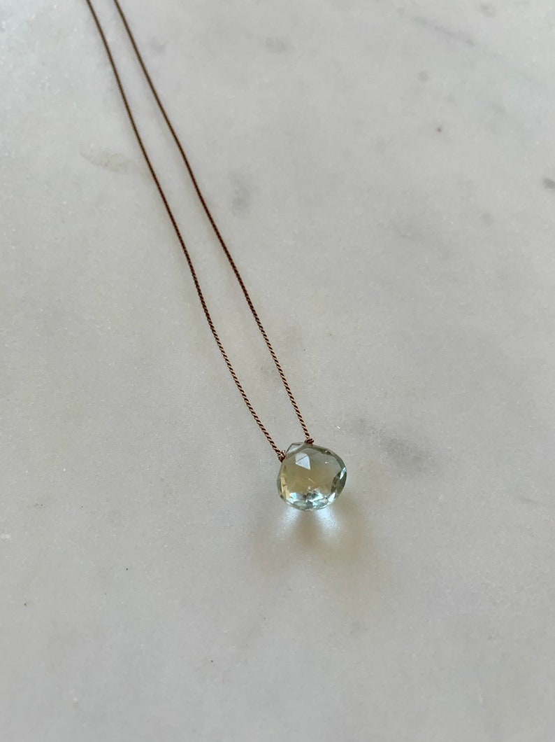 May include: A delicate necklace with a light green gemstone pendant on a brown cord.