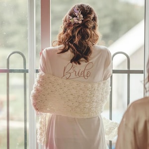 May include: A white bridal robe with a lace shawl and the word "Bride" written in pink script on the back.