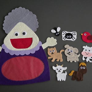 May include: A felt puppet set featuring a purple-clad woman with grey hair, a red bird, a spider, a fly, a brown cat, a white goat, a brown horse, a beige dog, and a black and white cow.