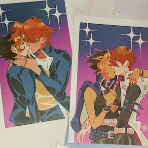 Könnte beinhalten: Zwei rechteckige Kunstdrucke mit Anime-Illustrationen von sich küssenden Charakteren. Der linke Druck zeigt Charaktere in dunklen Jacken vor einem violett-blauen Farbverlaufshintergrund mit Sternen. Der rechte Druck zeigt Charaktere in detaillierten Outfits.
