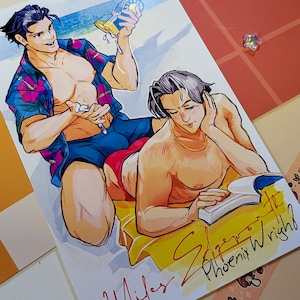 Puede incluir: Una impresión artística rectangular que muestra a dos personajes en una playa. Uno viste una camisa azul con flores y pantalones cortos azul oscuro, sosteniendo una botella amarilla. El otro viste pantalones cortos rojos y lee un libro. El texto dice Miles y Phoenix Wright.