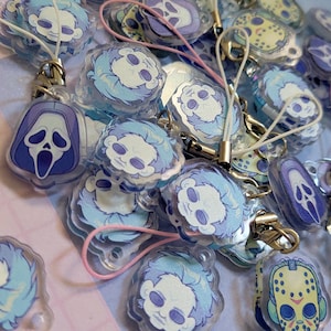 May include: A pile of acrylic charms with horror movie character designs. The charms are in shades of blue and purple, with clear backgrounds and keychains. Some charms feature the Ghostface mask from the Scream franchise.